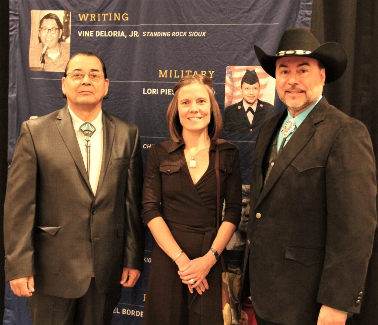 Three people standing in front of a military banner.