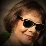 A woman wearing sunglasses and smiling for the camera.