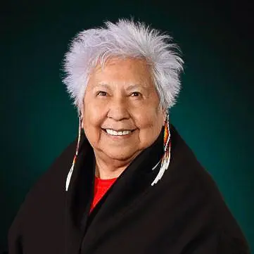 A woman with white hair and wearing feathers.