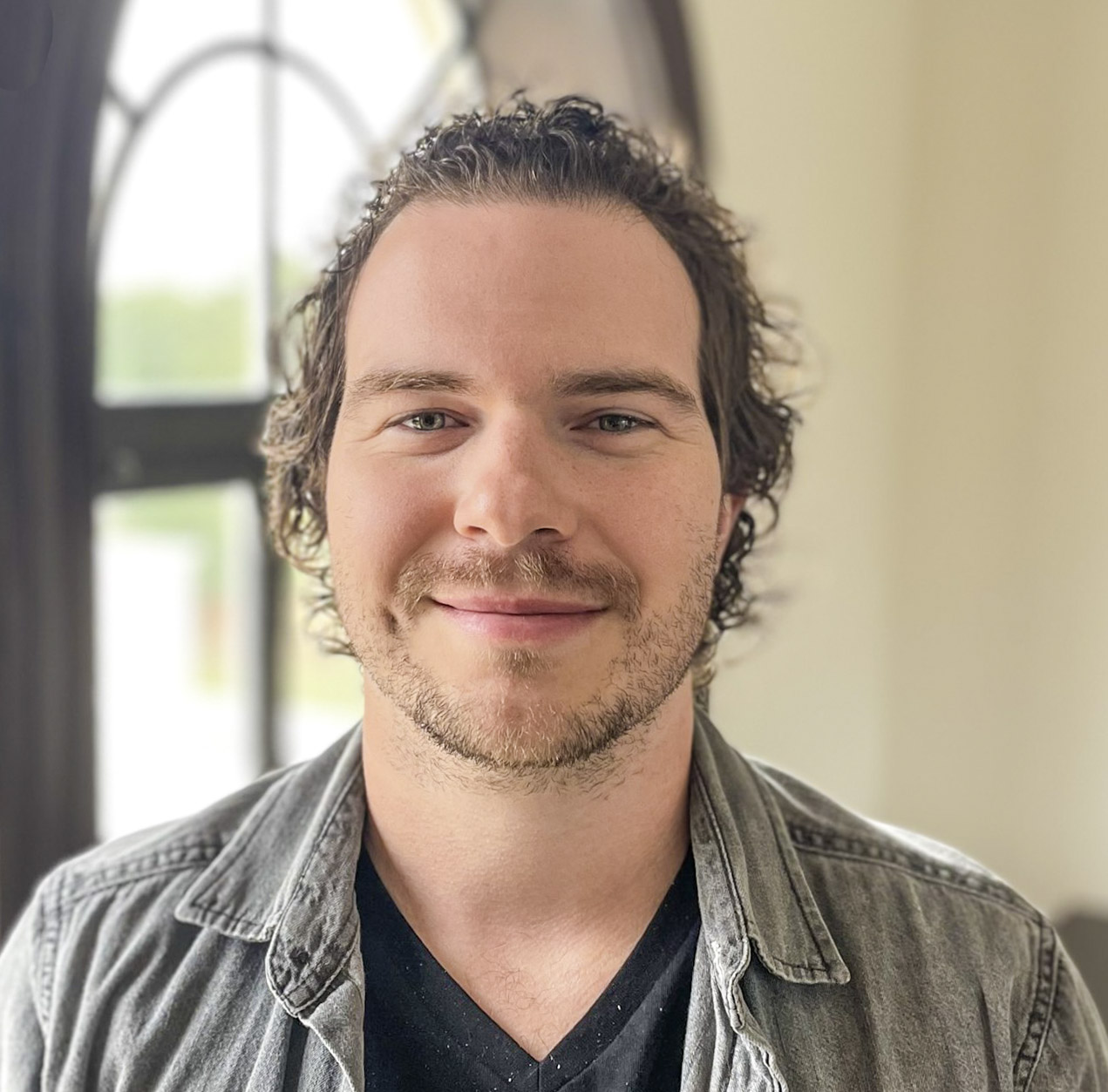 Smiling man with curly hair in casual attire.